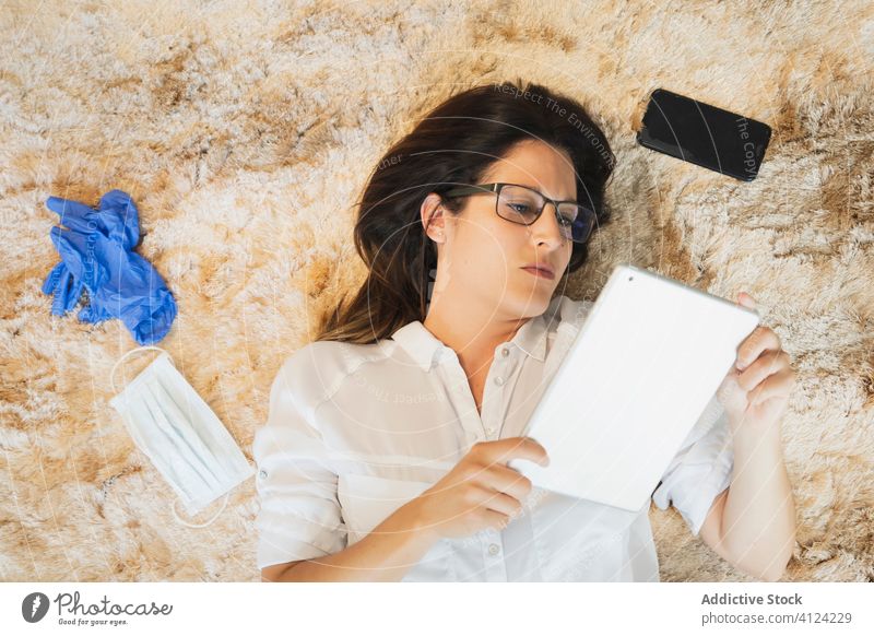 Junge Frau mit Schutzmaske und Handschuhen bei der Verwendung einer Tablette Coronavirus benutzend Mundschutz zu Hause bleiben Arbeit behüten Lügen Bett ernst