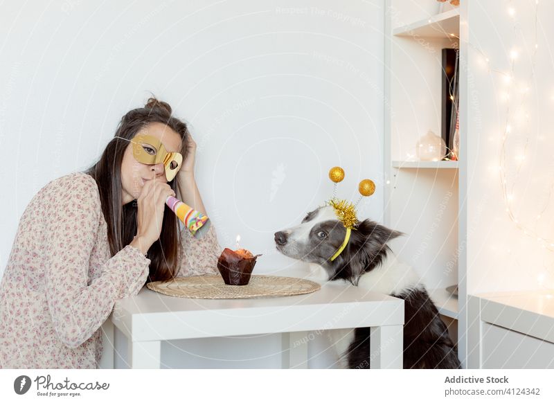Frau feiert Geburtstag mit Hund während der Quarantäne zu Hause feiern Coronavirus heimwärts Selbstisolierung Party Muffin Spaß haben Mundschutz Gebläse Hupe