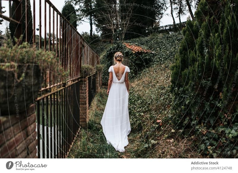 Anonyme Braut, die in der Nähe des Zauns im Garten spazieren geht Frau Spaziergang Hochzeit elegant Sommer romantisch Veranstaltung Kleid weiß grün Metall