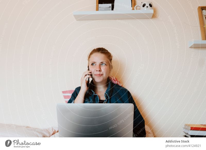 Millennial-Frau telefoniert, während sie zu Hause einen Laptop benutzt Smartphone Anruf heimwärts verwenden sich[Akk] entspannen Gespräch Bett Barfuß reden