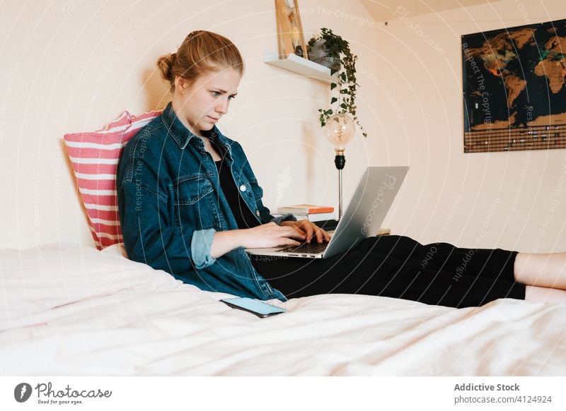 Junge Frau, die einen Computer benutzt, während sie in einem hellen Schlafzimmer chillt Laptop heimwärts verwenden sich[Akk] entspannen Bett Fuß Barfuß