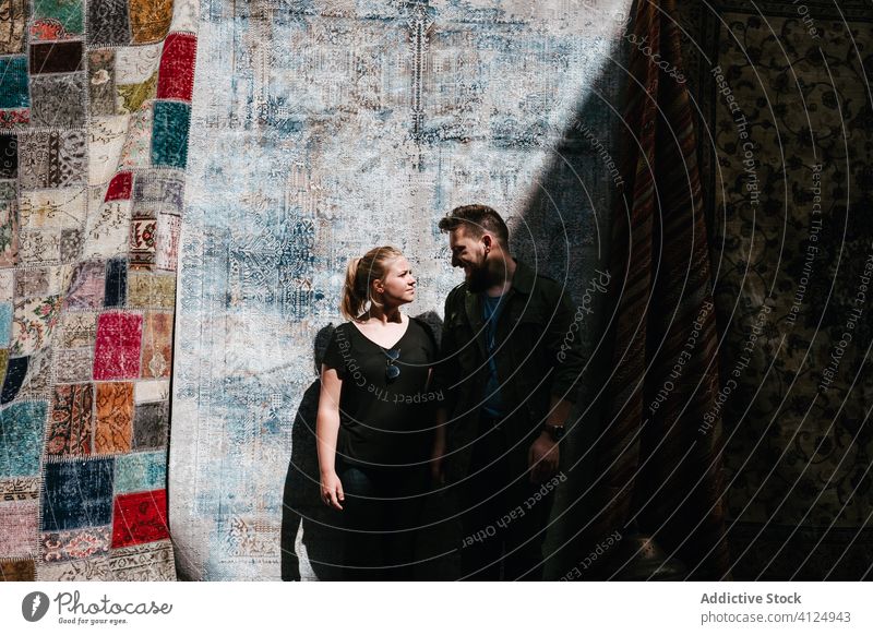 Glückliches Paar neben türkischen Teppichen stehend Tourist Umarmung gewebt Lachen Türkisch Zusammensein Ornament Markt Schatten Sommer Liebe lässig Outfit