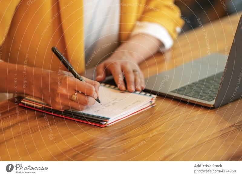 Geschäftsfrau macht sich Notizen in einem Notizblock, während sie in einem modernen Büro an einem Laptop arbeitet schreiben Hand Schreibstift Frau Handschrift