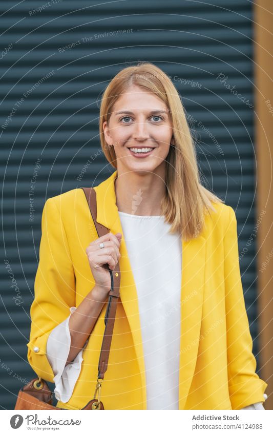 Fröhliche stilvolle Frau mit Handtasche über der Schulter auf der Straße Jacke Lächeln Freude Mode Outfit blond Glück charmant zufrieden freiberuflich Stil