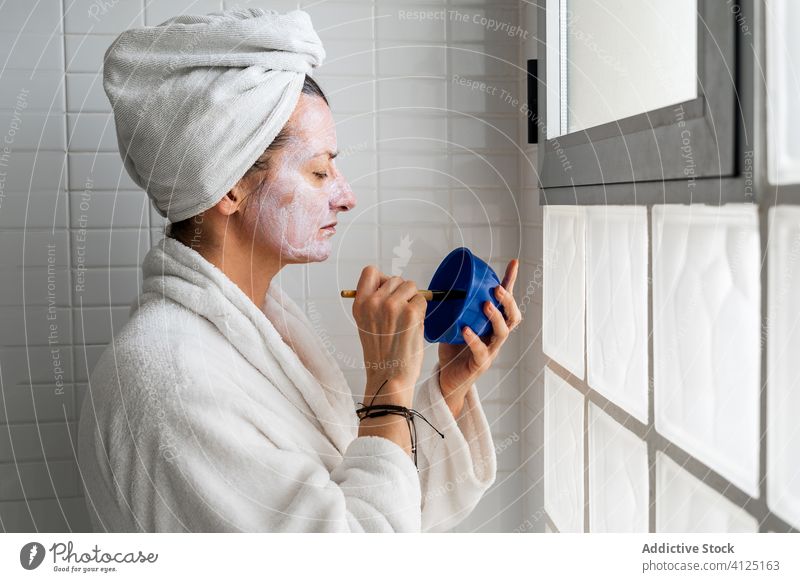 Frau mit Schale mit Kosmetikmaske im Badezimmer Gesichtsbehandlung Mundschutz Schalen & Schüsseln Bürste Hautpflege Ton bewerben Bademantel Handtuch Turban