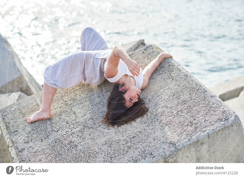 Junge Frau liegt auf einem Steinbau in Meeresnähe Ufer Wellenbrecher sinnlich Tänzer Beton Lügen Zeitgenosse Konzept MEER modern Verlockung Körper genießen jung