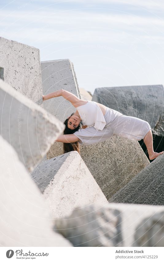 Junge Frau sitzt auf einer Steinkonstruktion Beton Tanzen sinnlich Kraft Natur Harmonie Zeitgenosse Ufer Küste Konstruktion schieben modern Konzept anstrengen