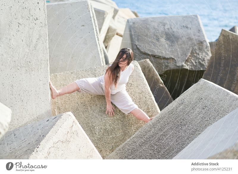 Junge Frau sitzt auf einer Steinkonstruktion Beton Tanzen sinnlich Kraft Natur Harmonie Zeitgenosse Ufer Küste Konstruktion schieben modern Konzept anstrengen