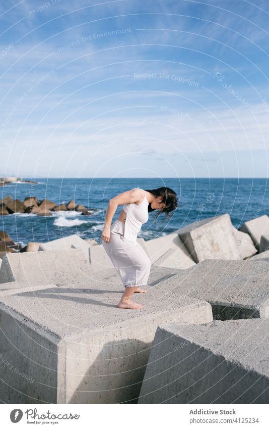Moderne Frau steht auf Betonblock des Wellenbrechers MEER Tanzen sinnlich Kraft Harmonie Küste Zeitgenosse Konzept Stein Konstruktion Energie physisch jung Pose