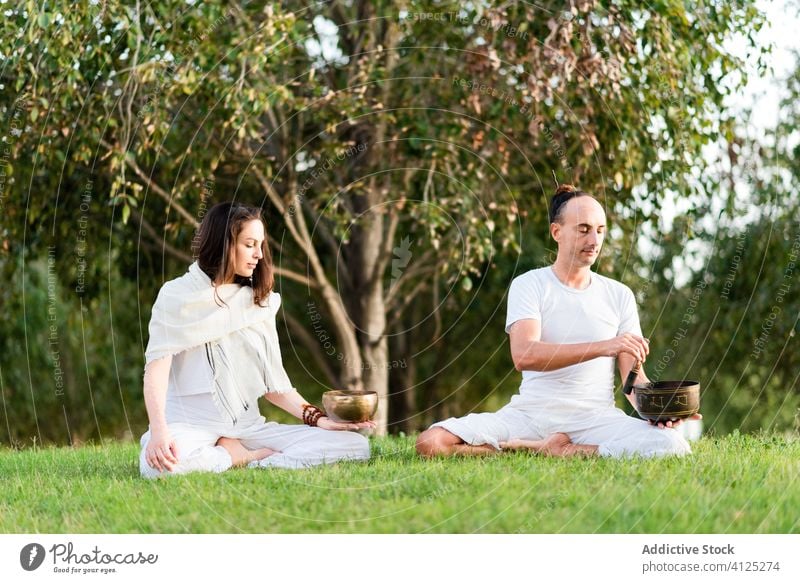Konzentriertes Paar beim Meditieren im Lotussitz Yoga Klangschale tibetische Schale beweglich Lotus-Pose meditieren Windstille Augen geschlossen Zen Rasen