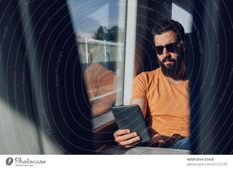 Bärtiger Mann mit Sonnenbrille surft im Zug auf seinem Smartphone Tablette Passagier Arbeitsweg reisen Sommer Mobile Telefon Browsen Verkehr Fenster Vollbart
