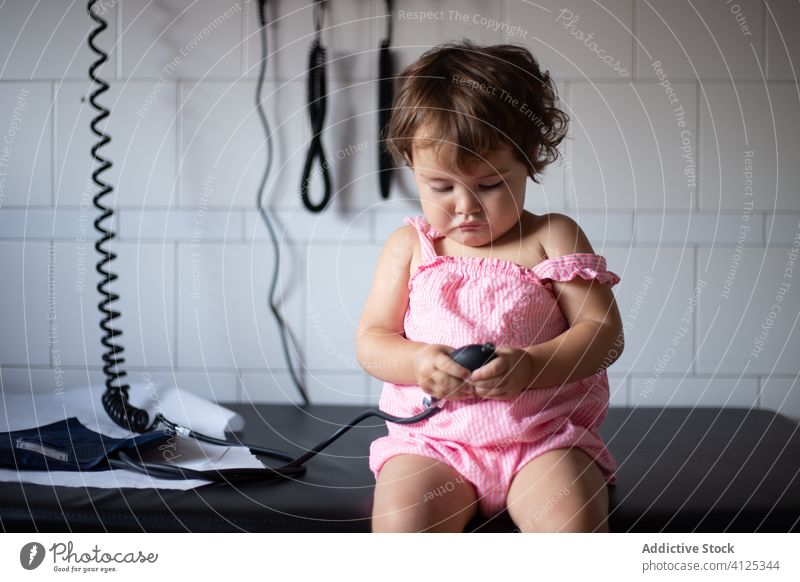 Neugieriges kleines Mädchen spielt mit Tonometer in der Klinik Instrument geduldig wenig Kleinkind prüfen spielen niedlich sitzen Kind Gerät Virus Bund 19