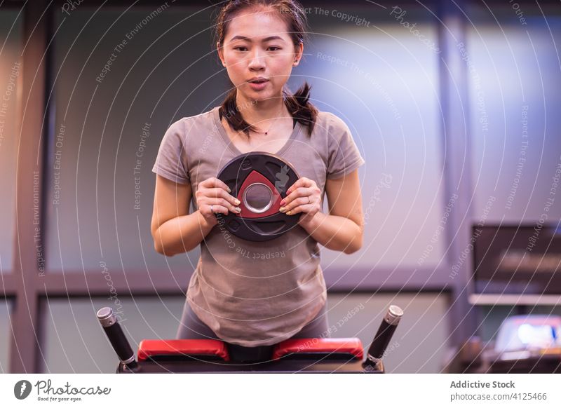 Ernsthafte asiatische junge Sportlerin bei einer Übung mit Gewichten auf einer Bank in einem modernen Fitnessstudio Training Hyperextension stark Athlet
