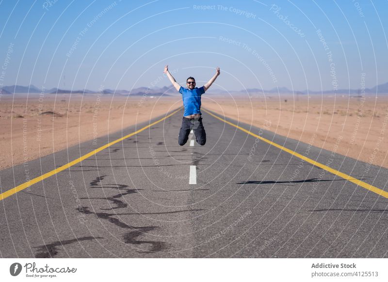 Aufgeregter junger Mann springt auf Asphaltstraße aufgeregt Abenteuer Freiheit reisen wüst Straße springen Sprung Saudi-Arabien männlich Glück heiter