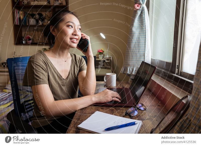 Beschäftigte Unternehmerin, die auf einem Laptop tippt und ein Mobiltelefon benutzt Tippen Smartphone Frau heimwärts Büro beschäftigt benutzend asiatisch