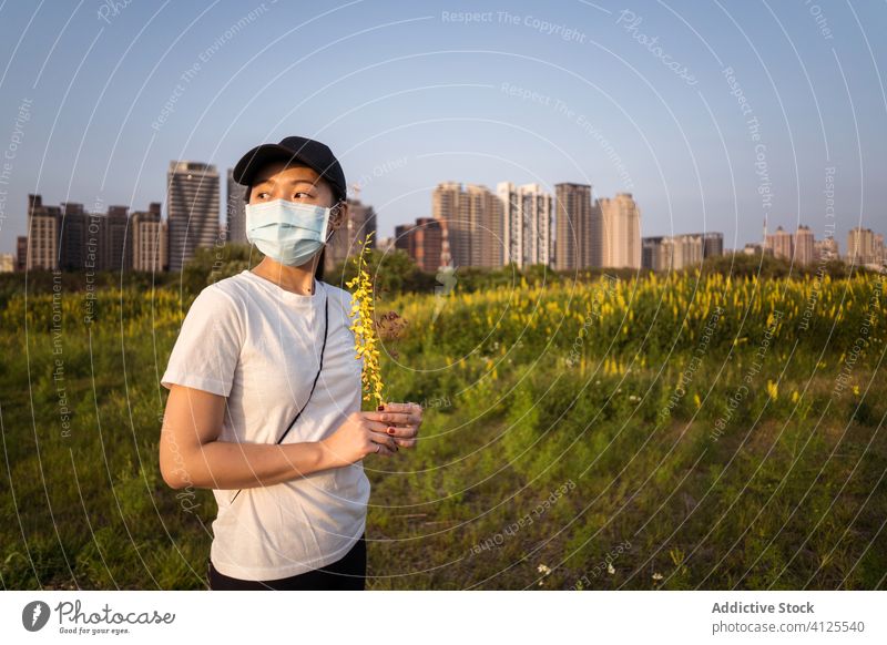 Ethnische Frau mit medizinischer Maske steht auf grünem Feld Mundschutz behüten Coronavirus verhindern COVID Natur jung lässig ethnisch modern Sicherheit