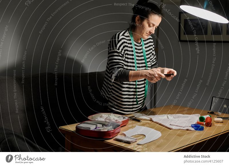 Frau, die den Nähvorgang fotografiert Designer fotografieren Smartphone Gewebe hölzern Näherin nähen Muster Spielfigur detai Tisch Arbeit Arbeitsplatz heimwärts