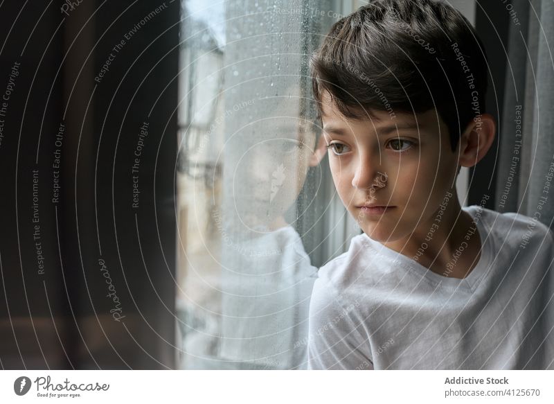 Unaufgeregter Junge schaut zu Hause aus dem Fenster gelangweilt beobachten Regen Wohnzimmer heimwärts Straße emotionslos Kind verträumt nachdenklich stehen