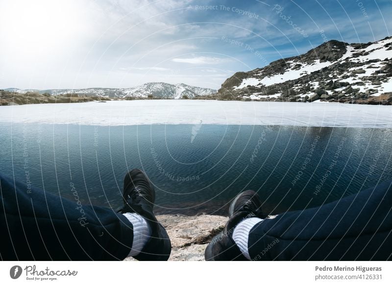 Füße eines Mannes sitzen vor einem gefrorenen See in der Spitze eines verschneiten Berges. Peñalara Gipfel Madrid Natur Schnee Eis Winter Person Freizeit