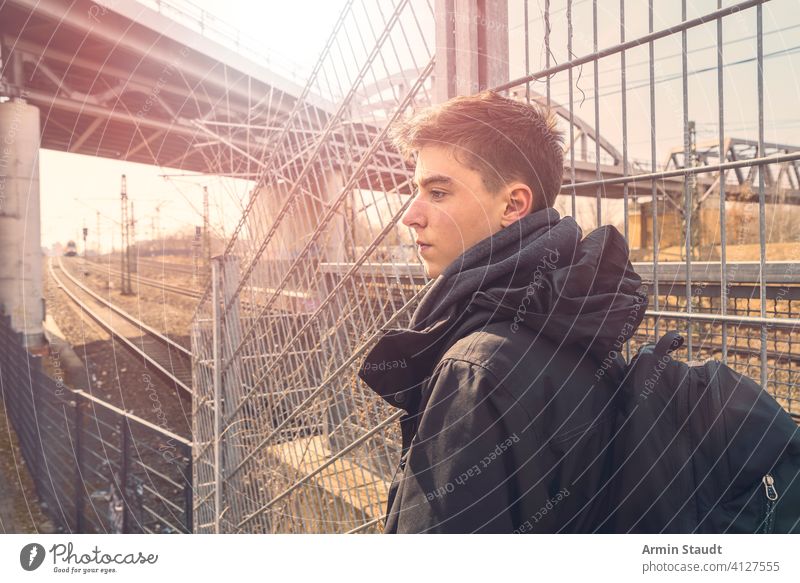Ernster junger Mann mit Rucksack auf Reisen, die Eisenbahn im Hintergrund Spuren Landschaft im Freien ernst selbstbewusst müde allein Tourist Tourismus Schiene