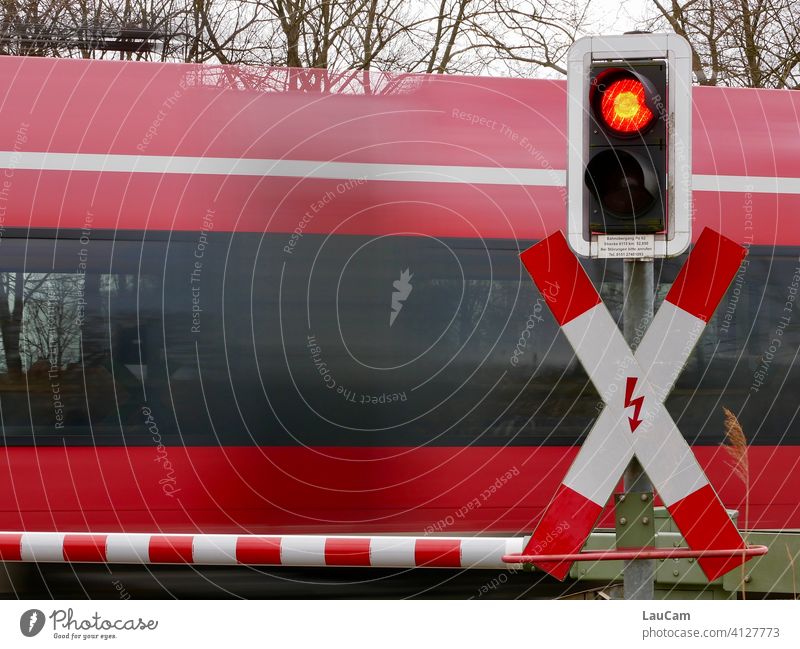 Ein roter Zug rauscht an einem geschlossenen Bahnübergang mit rot-weißer Schranke und roter Ampel vorbei Bahnfahren rote Ampel Verkehr Eisenbahn Gleise