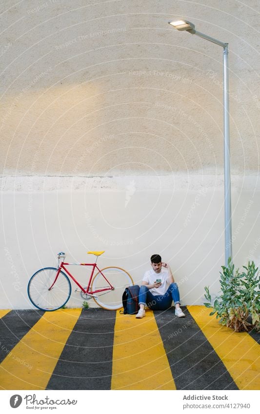 Mann auf dem Boden sitzend mit einem Fahrrad Fixie Zyklus urban Rad feststehend Sport Transport Ausrüstung Lifestyle Wand Straße Hipster Mitfahrgelegenheit