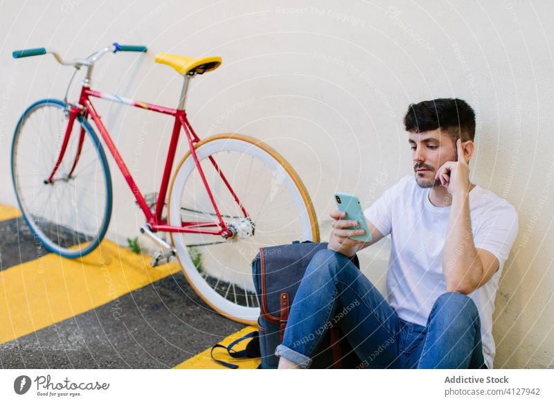 Mann überprüft sein Smartphone auf der Straße sitzend Fahrrad Fixie Zyklus urban Rad feststehend Sport Transport Ausrüstung Lifestyle Wand Hipster