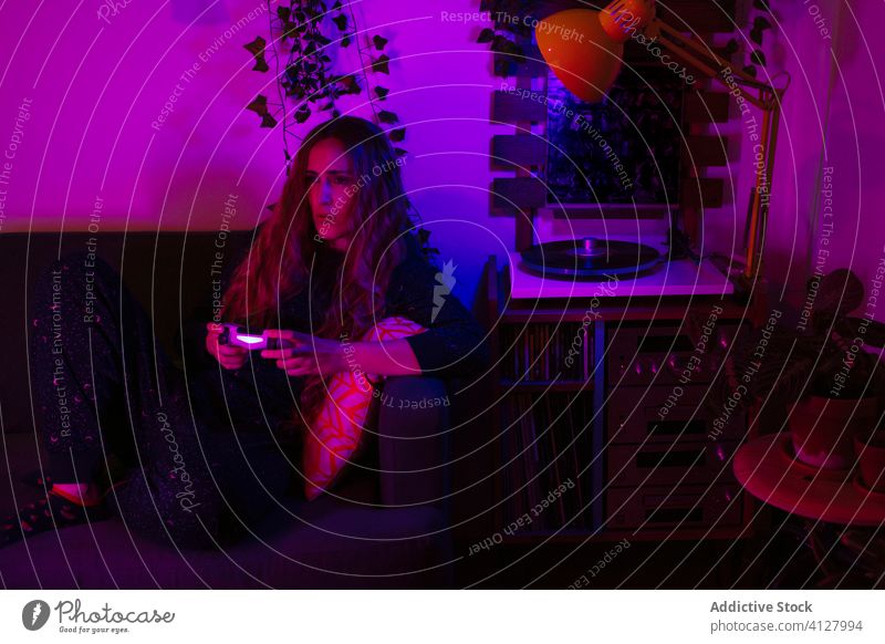 Konzentrierte Frau spielt Videospielkonsole auf dem Sofa zu Hause Gamepad spielen Nacht neonfarbig spät unterhalten Erholung Freizeit heimwärts benutzend