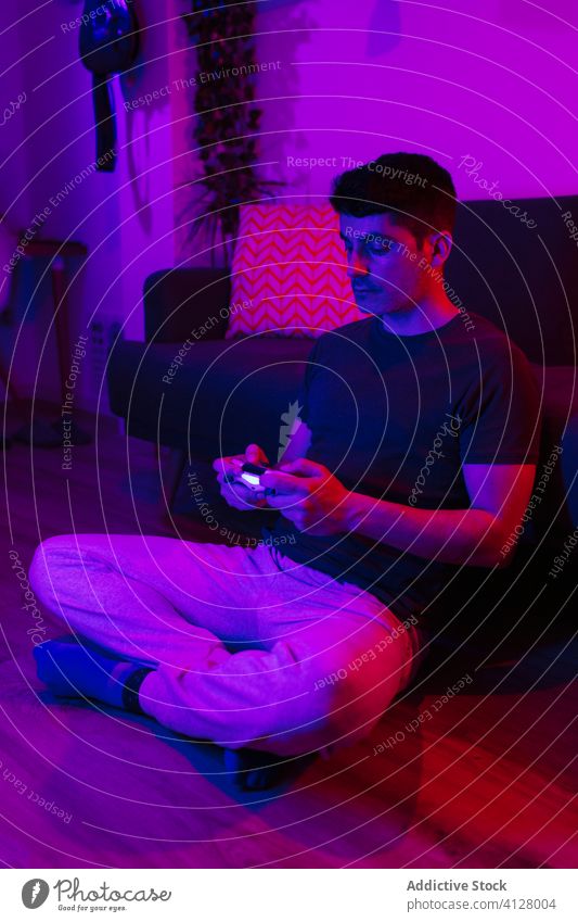 Mann benutzt Spielkonsole in Wohnung Gamepad spielen unterhalten Nacht heimwärts neonfarbig Spieler spät Erholung Freizeit sitzen Beine gekreuzt benutzend