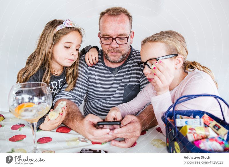 Vater und Töchter nutzen Smartphone am Tisch Tochter benutzend Banane Kinder Geschwisterkind essen Zusammensein heimwärts Mann Mädchen wenig Browsen Gerät