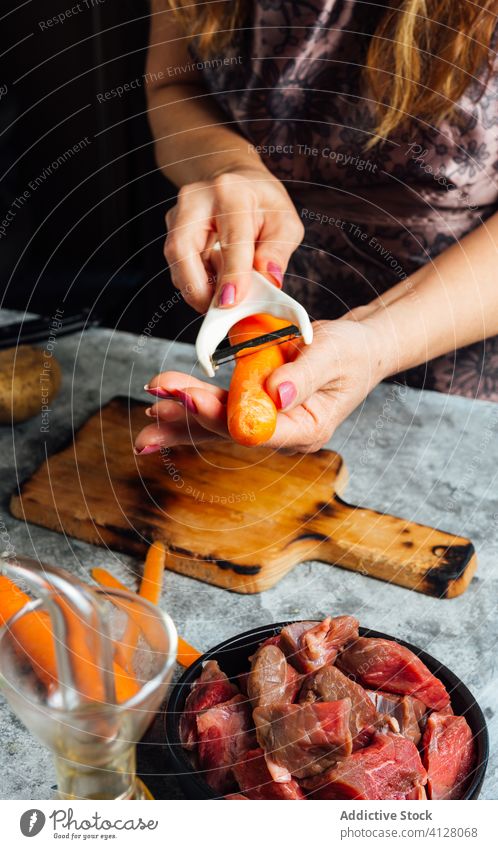 Köchin schält frische Karotten in der Küche sich[Akk] schälen Möhre Schäler Frau Koch Schneidebrett Gemüse vorbereiten Abendessen Hausfrau Tisch Lebensmittel