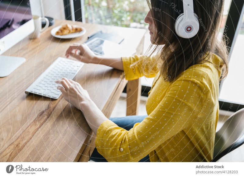 Konzentrierte Frau am Computer zu Hause Keyboard Telearbeit Schreibtisch pc Kopfhörer freiberuflich Tippen benutzend Tablette Croissant Kaffee Browsen online