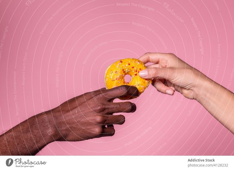Crop multiethnischen Menschen halten Donut auf rosa Hintergrund Doughnut Paar Hand frisch lecker Dessert geschmackvoll Snack Halt genießen Freizeit Zusammensein