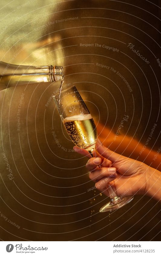 Anonyme Person gießt Champagner aus der Flasche in ein Glas auf goldenem Hintergrund Hand Halt Weinglas eingießen Alkohol feiern trinken Feiertag Veranstaltung