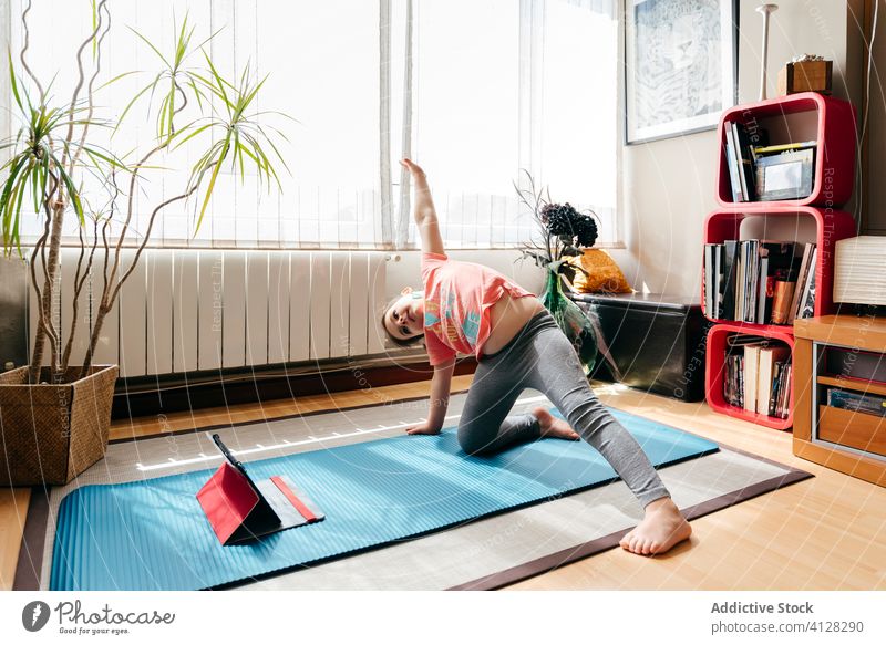 Fröhliches kleines Mädchen macht Yoga wilde Sache Pose Kind Unterlage Wildes Ding Pose Video Tablette camatkarasana Tutorial Gleichgewicht üben zu Hause