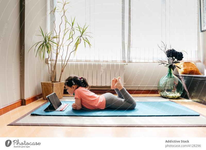 Kleines Mädchen ruht sich nach Yoga im hellen Raum aus ruhen Kind Unterlage Video Tablette liegend Tutorial üben zu Hause Stressabbau zuschauen Harmonie Sprit