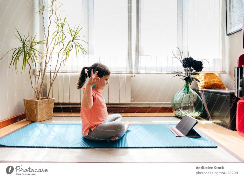 Barfuß Mädchen tun Meditation in gemütlichen Raum zu Hause Kind Yoga Lotus-Pose Konzentration Zen Sprit meditieren Tablette Tutorial Video Unterlage Frieden