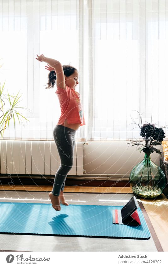 Nettes Mädchen übt Yoga im Wohnzimmer zu Hause springen Energie Kind Unterlage hochreichen Video Tablette Tutorial Barfuß Wellness Vitalität Gleichgewicht üben