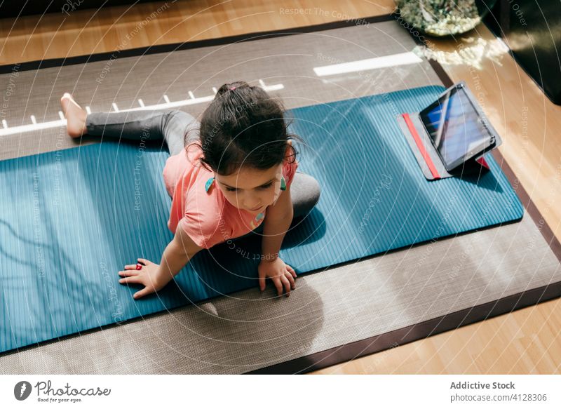 Kleines Mädchen macht Yoga im hellen Raum Kind Pose Unterlage Video Tablette Tutorial Gleichgewicht üben zu Hause Stressabbau zuschauen Harmonie Dehnung