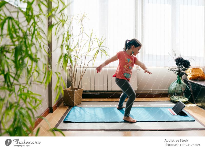 Fröhliches kleines Mädchen macht Yoga im hellen Raum Kind Pose Unterlage Video Tablette Tutorial Gleichgewicht üben zu Hause Stressabbau zuschauen Harmonie