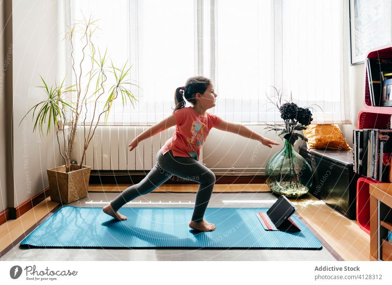 Kleines Mädchen übt Yoga in der Zwei-Krieger-Pose Kind Asana üben heimwärts Krieger zwei Tablette virabhadrasana online beweglich Dehnung wenig Unterlage