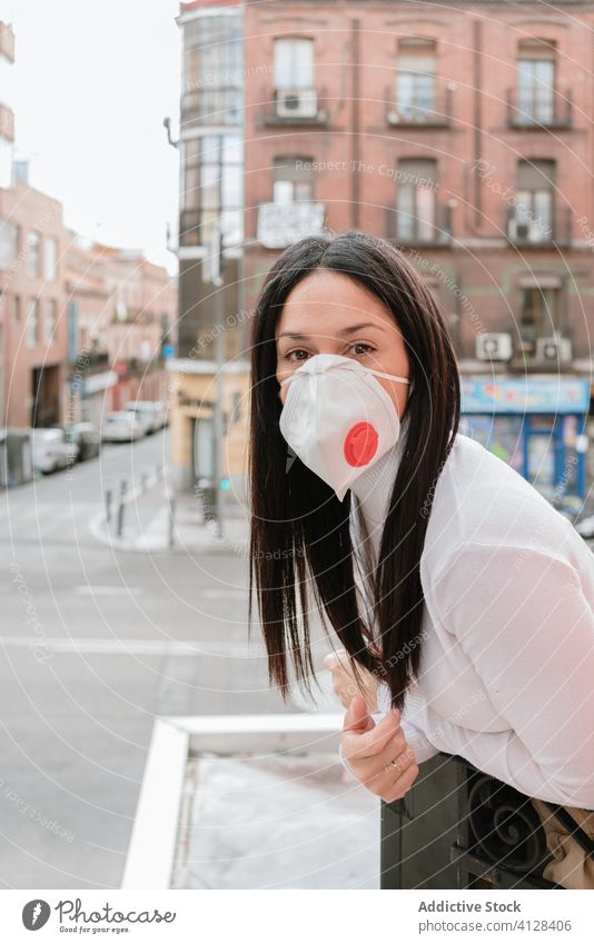 Junge Frau mit Atemschutzmaske steht auf einem Balkon Coronavirus heimwärts Mundschutz COVID Pandemie Großstadt Selbstisolierung Quarantäne Sperrung