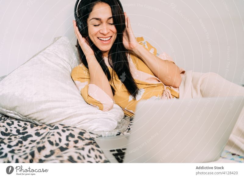 Glückliche Frau mit Laptop und Kopfhörern auf dem Bett Musik zuhören Kälte genießen Komfort räkeln Schlafzimmer sich[Akk] entspannen Lifestyle ruhen Apparatur