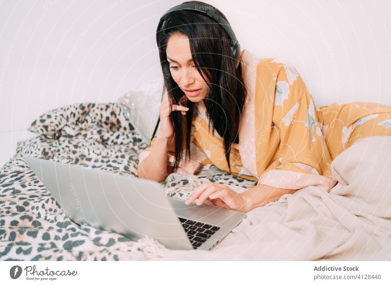 Frau mit Laptop und Kopfhörern auf dem Bett Musik zuhören Kälte Glück genießen Komfort räkeln Schlafzimmer sich[Akk] entspannen Lifestyle ruhen Apparatur Gerät