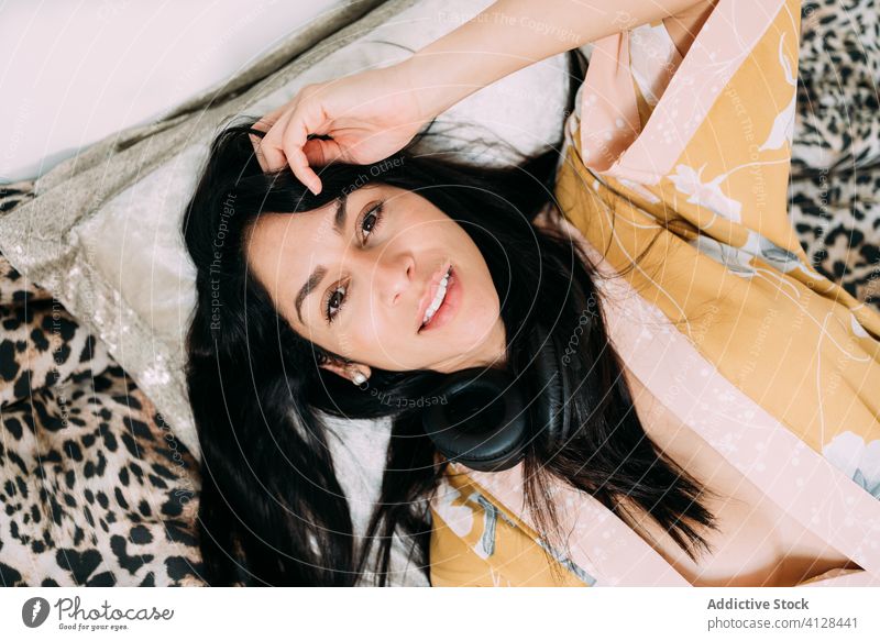 Glückliche Frau, die mit Kopfhörern auf dem Bett liegt aussruhen Musik Kälte genießen Komfort räkeln Schlafzimmer sich[Akk] entspannen Lifestyle Apparatur Gerät