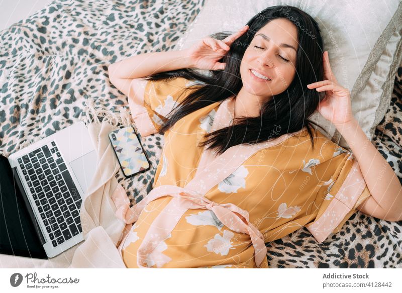 Glückliche Frau mit Laptop und Kopfhörern auf dem Bett Musik zuhören Kälte genießen Komfort räkeln Schlafzimmer sich[Akk] entspannen Lifestyle ruhen Apparatur