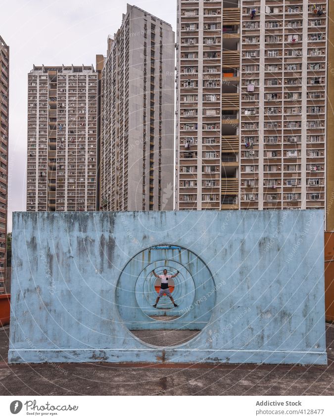 Fröhlicher Mann, der auf einer Mauer mit Tunnel in Hongkong steht Stehen Straße Wand Stollen Kondominium Hof heiter Großstadt Gebäude Appartement männlich