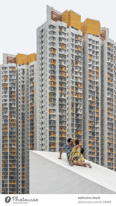 Paar küsst sich auf schrägem Dach vor Hochhäusern in Hongkong Wolkenkratzer Gebäude wohnbedingt Höhe Kuss Küssen Liebe Spaß haben Berghang mehrstöckig