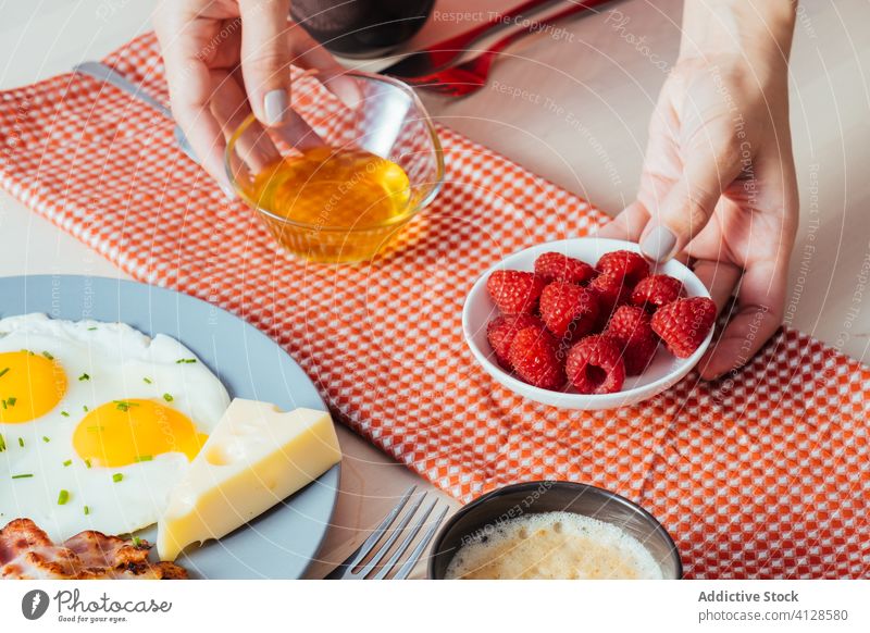 Anonyme Erntehelfer stellen zum Frühstück Teller mit Himbeeren und Honig auf den Tisch Liebling geschmackvoll Lebensmittel Hand Morgen süß frisch Gesundheit