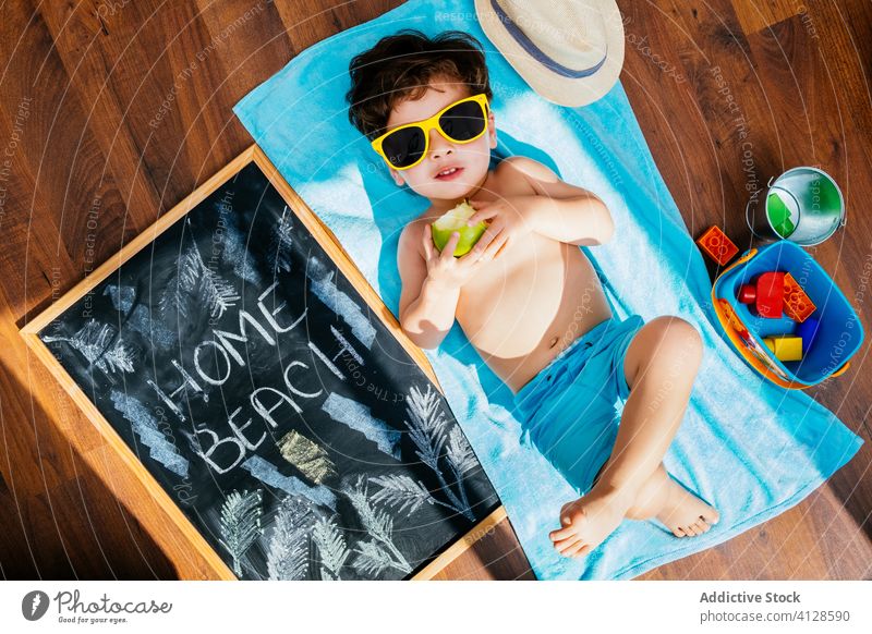 Glücklicher kleiner Junge mit Sonnenbrille, der zu Hause am Strand sitzt und vom Sommer träumt heimwärts Selbstisolierung Spaß träumen soziale Distanzierung